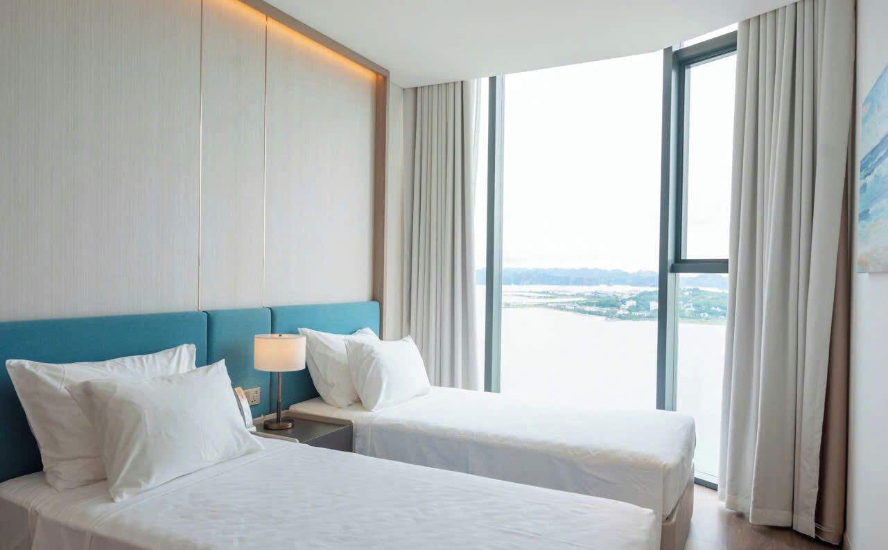A hotel room with two beds, a view of a cityscape, and a large window with curtains.