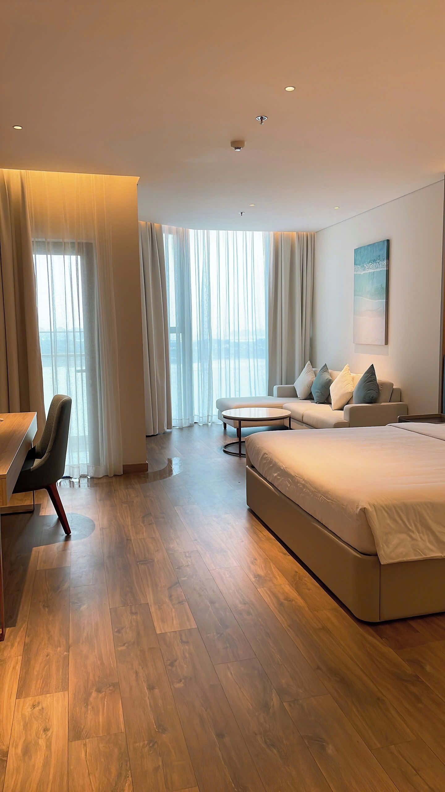Una habitación de hotel moderna con una cama grande, un sofá, una mesa de comedor y vista al mar.