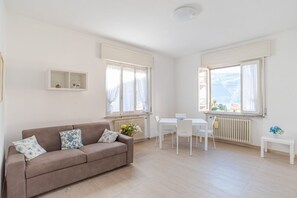 Una sala de estar moderna con sofá, mesa de comedor, sillas y ventanas grandes con cortinas.