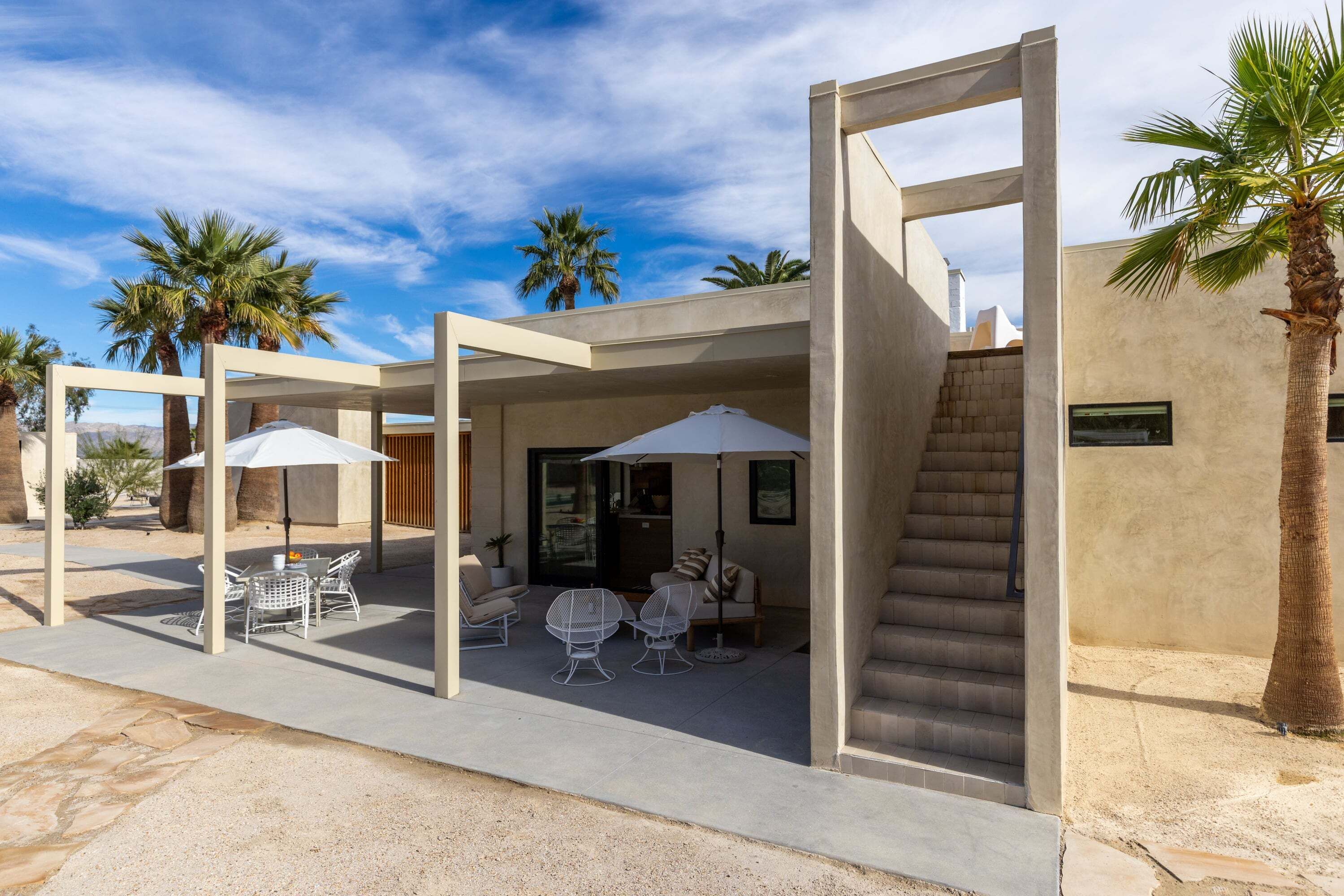 Ein moderner Außenbereich mit Terrasse, Sitzgelegenheiten, einer Treppe und Palmen.