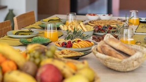 Uma mesa de café da manhã com diversas frutas, doces e suco de laranja.