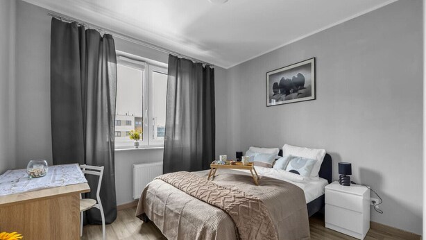 A modern bedroom with a bed, bedside table, and a desk with a chair. - Modern 1BR in Bemowo – Parking & Workspace (Warszawa)