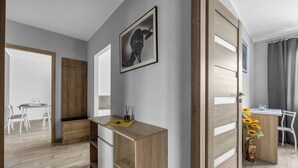 A modern room with a wooden desk, a dining area, and a large window. - Modern 1BR in Bemowo – Parking & Workspace (Warszawa)