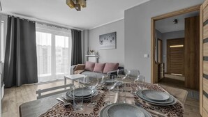 A modern living room with a dining area set for six. - Modern 1BR in Bemowo – Parking & Workspace (Warszawa)