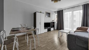 A modern living room with a dining area, a flat-screen TV, and a sofa. - Modern 1BR in Bemowo – Parking & Workspace (Warszawa)