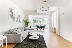 A modern living room with a grey sectional sofa, two round coffee tables, a large green rug, and a view of a patio with outdoor furniture. - Global Living Berlin Rosenthaler Platz (Berlin)