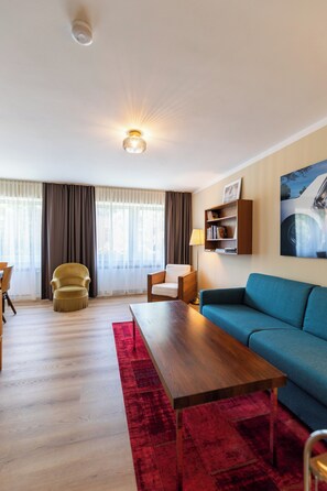 Een moderne woonkamer met een houten salontafel, een blauwe bank, een gele fauteuil, een rood vloerkleed en een boekenkast met een ingelijst kunstwerk.