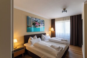 A hotel room with a large bed, two bedside lamps, a painting on the wall, and a window with curtains. - Luis City Apartments (Regensburg)
