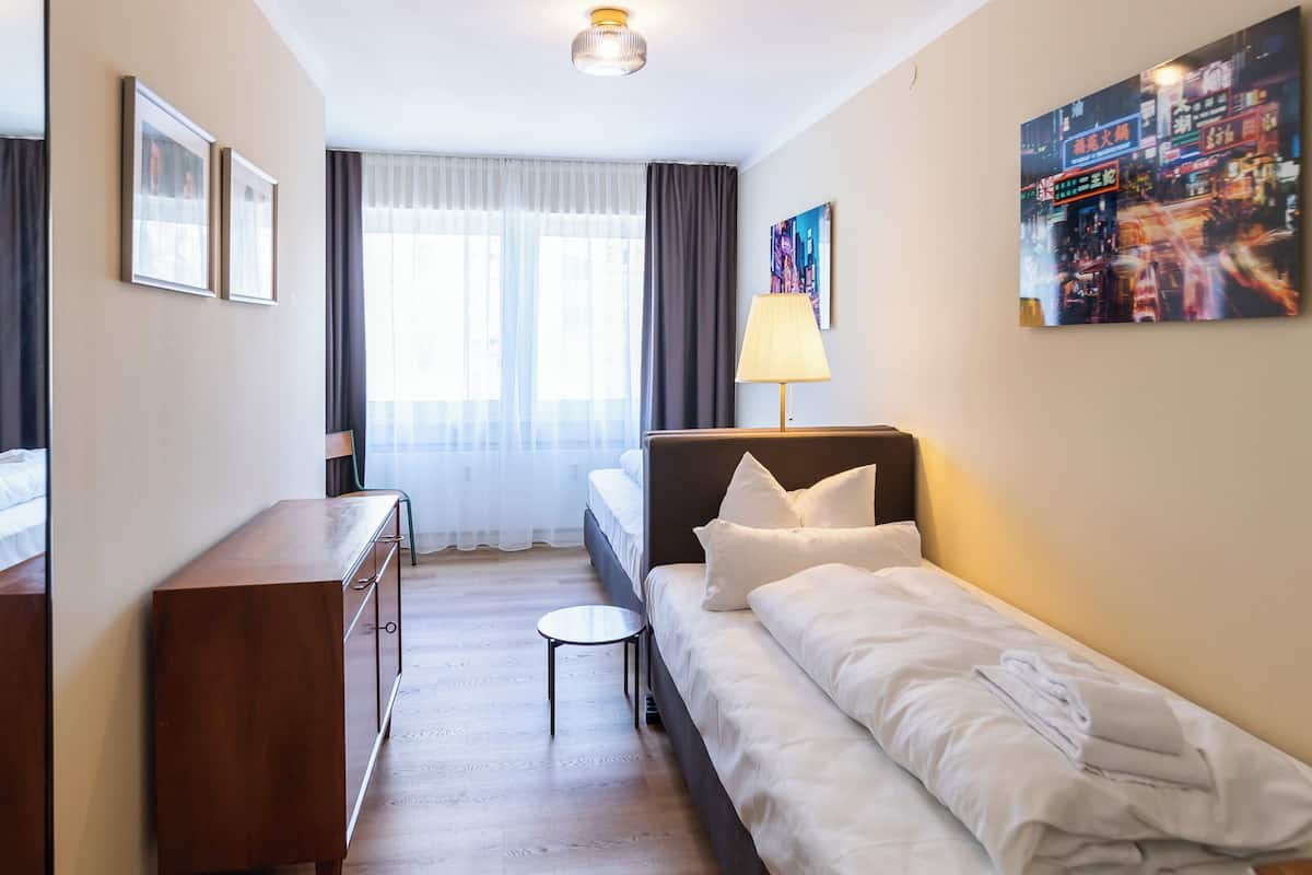 Ein Hotelzimmer mit Bett, Schreibtisch, Stuhl, Lampe, einem fenster mit Vorhängen und einer Deckenleuchte.