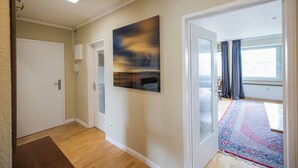 Een gang met een houten vloer, een deur, een glazen deur en een groot abstract schilderij aan de muur.