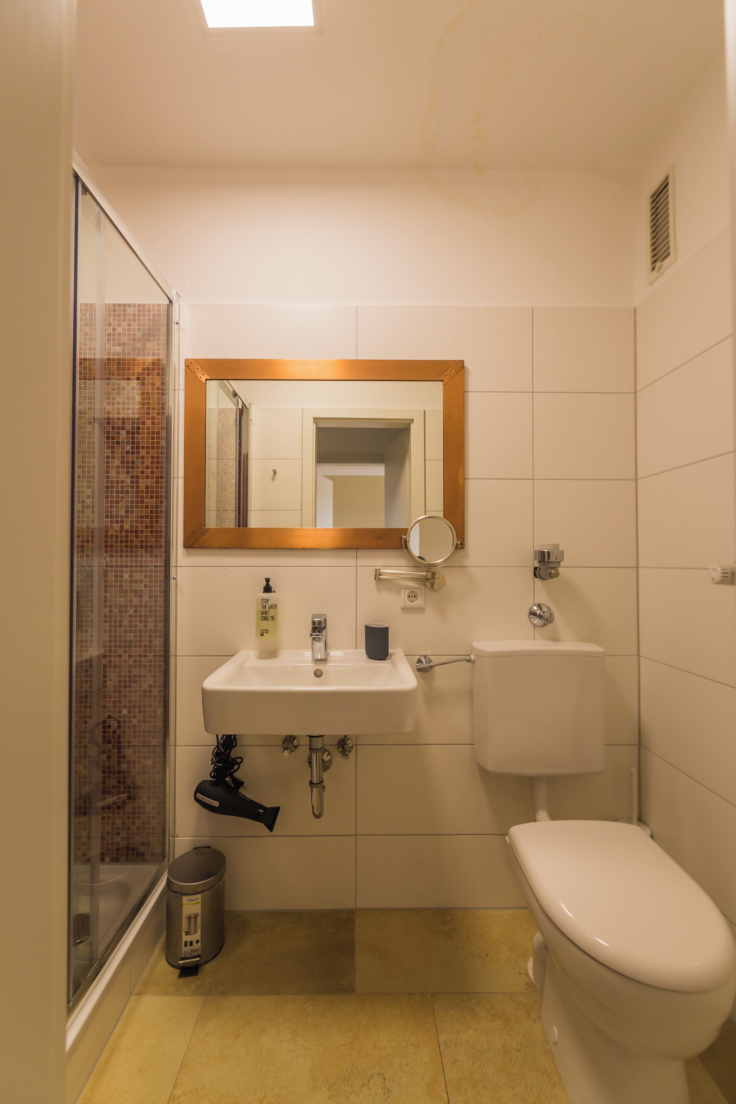 A bathroom with a shower, sink, toilet, and a mirror.