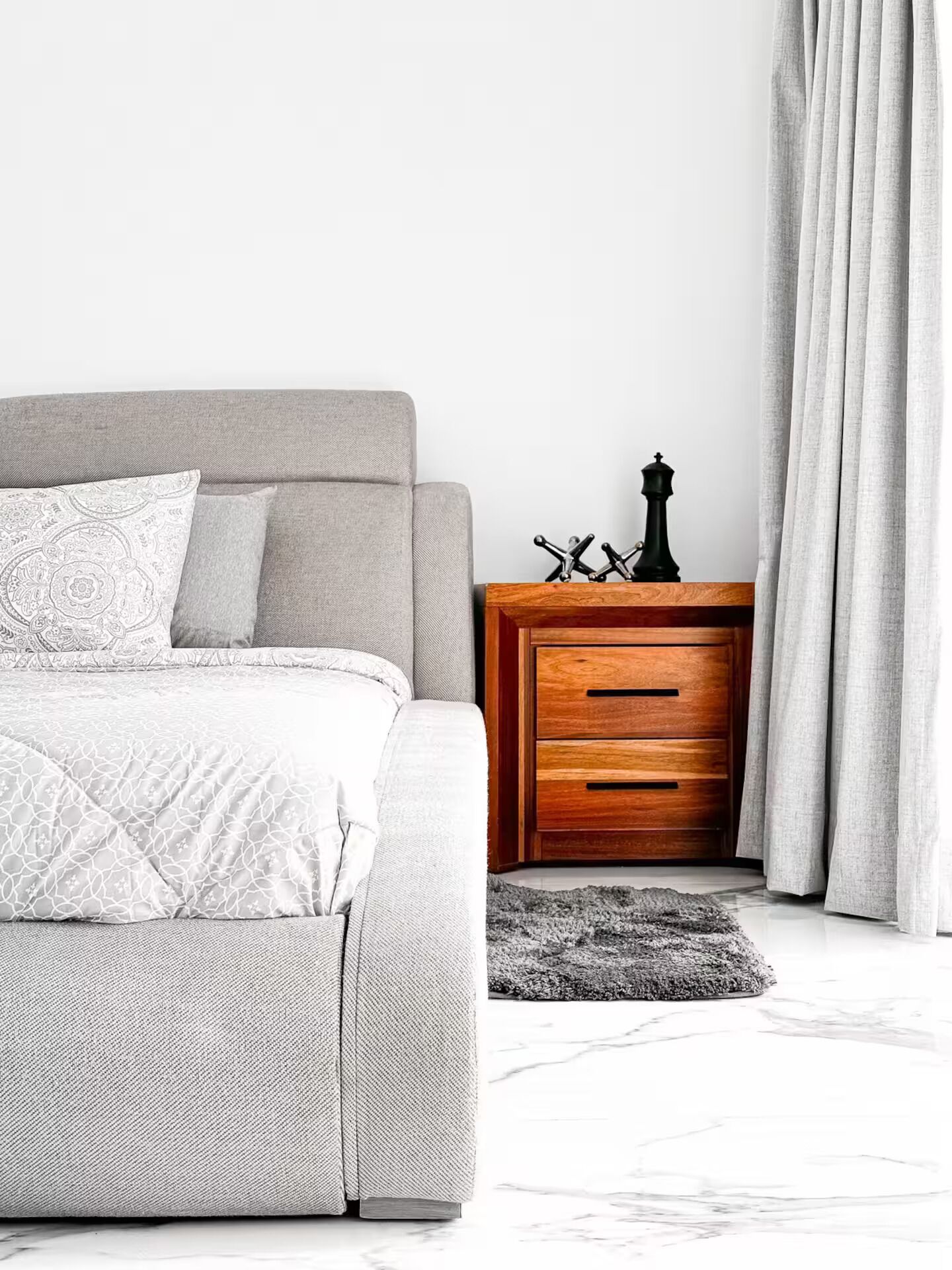 A modern bedroom with a grey sofa bed, a wooden nightstand with drawers, and a decorative black object on top.