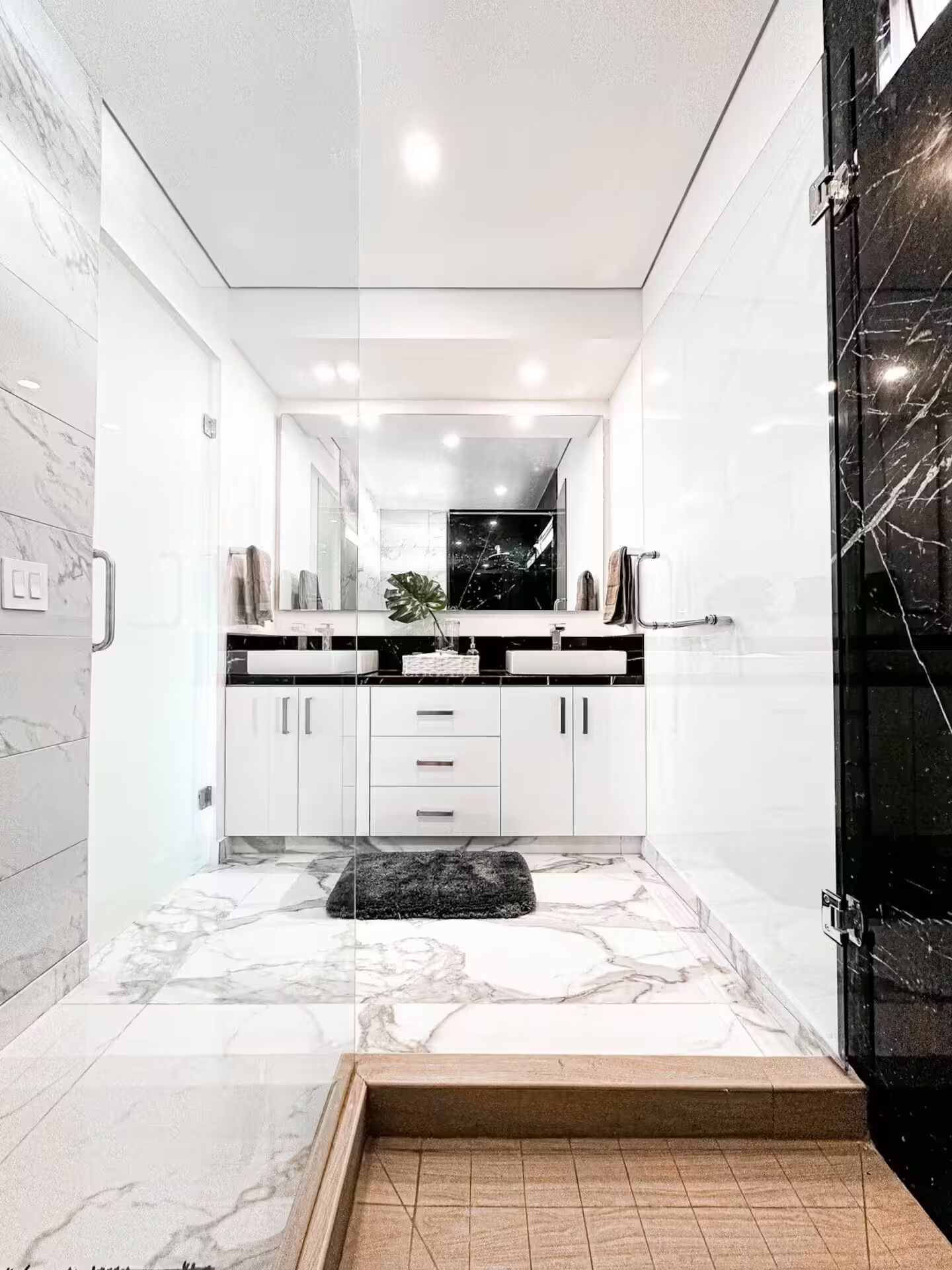 Een moderne badkamer met een grote spiegel, witte kastjes en een marmeren vloer.