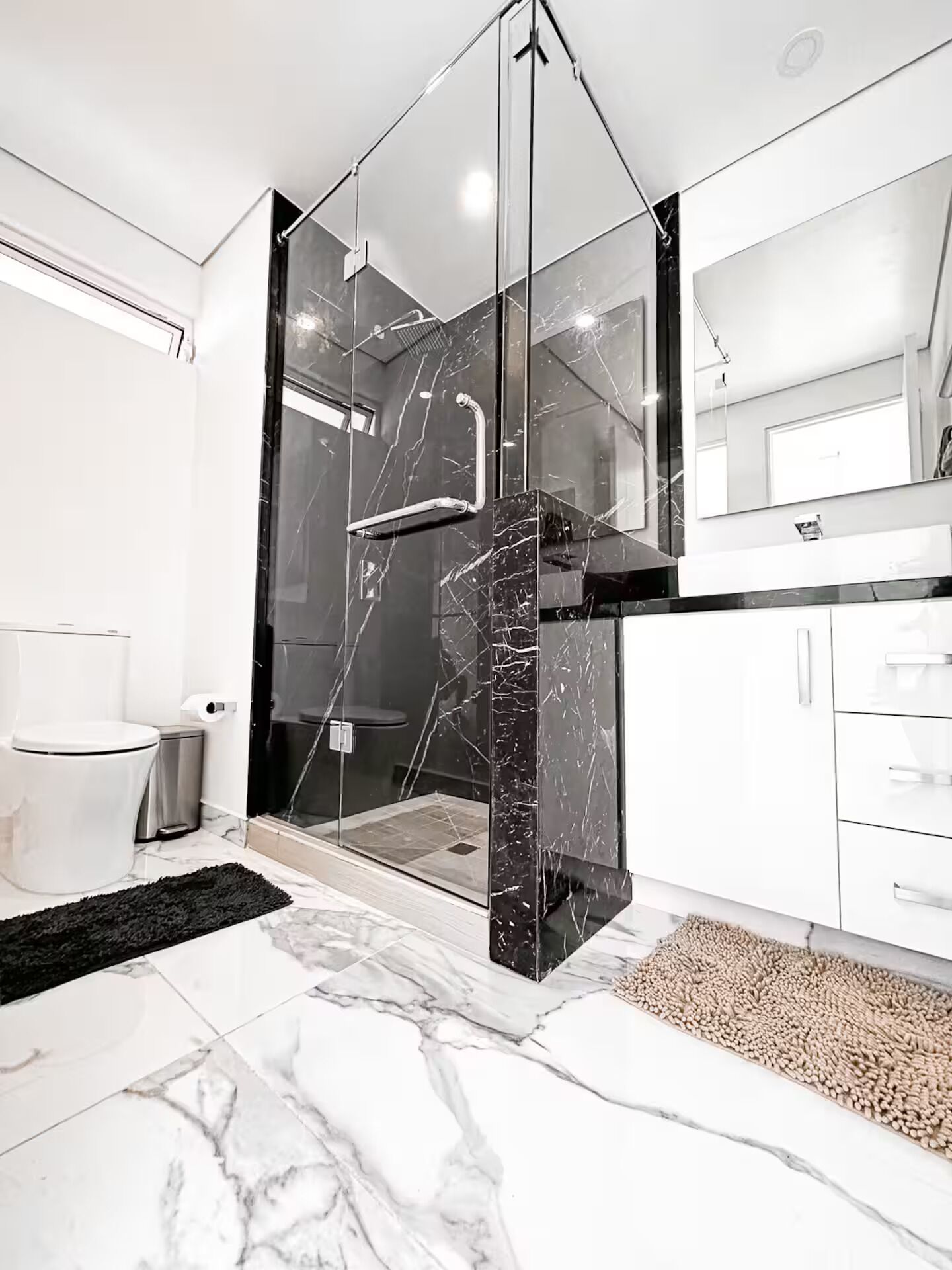 A modern bathroom with a glass-enclosed shower, marble flooring, and white cabinetry.