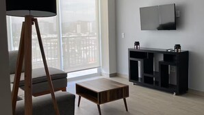 Ein modernes Wohnzimmer mit großem Fenster, Flachbildfernseher, Holz-Couchtisch und Stehlampe.