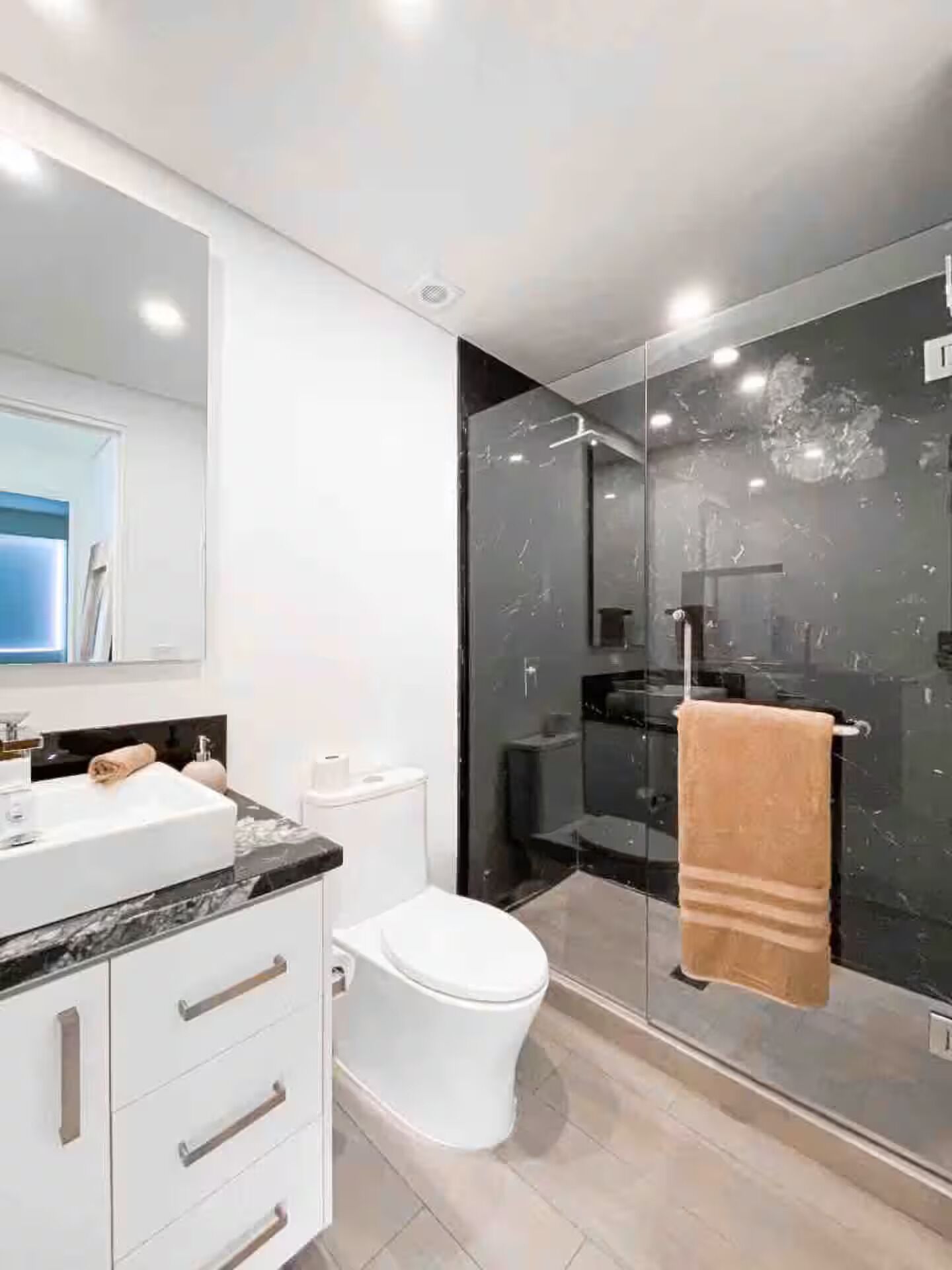 Un baño moderno con un lavamanos blanco, una ducha con mampara de vidrio y un inodoro blanco.