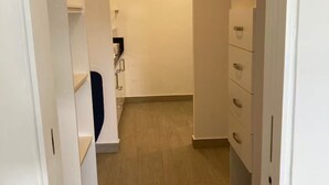 En smal hall med vita garderober på båda sidor, trägolv och en dörr som leder till ett annat rum.