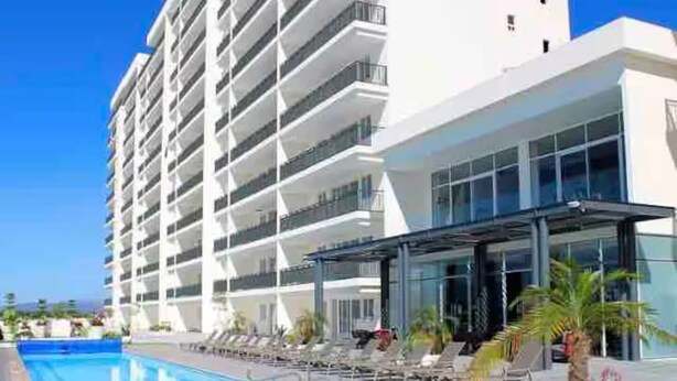 Ett modernt hotell med poolområde, solstolar och en möblerad, överbyggd uteplats.