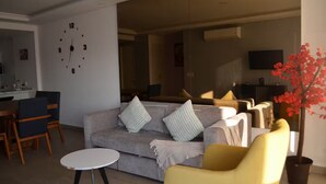 A modern living room with a grey sofa, a round coffee table, and a yellow armchair. There is a dining area with a wooden table and chairs, and a kitchen in the background. - Charming apartment, incredible view (Zapopan)