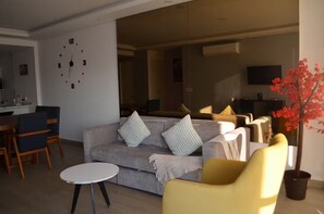 A modern living room with a grey sofa, a round coffee table, and a yellow armchair. There is a dining area with a wooden table and chairs, and a kitchen in the background. - Charming apartment, incredible view (Zapopan)