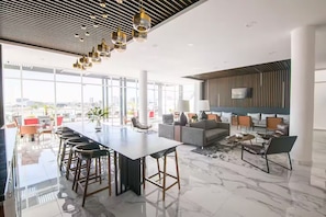 Un intérieur moderne avec un long bar, un espace salon et de grandes fenêtres offrant une vue sur la ville.