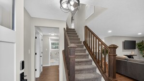 A staircase with wooden railings, a hallway with a door, and a living area with a sofa and a television. - Beaverton Escape, Backyard & Game Room (Beaverton)