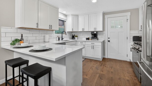 A modern kitchen with white cabinetry, a central island with stools, a built-in oven, and a refrigerator. - Beaverton Escape, Backyard & Game Room (Beaverton)