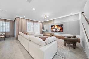 A modern living room with a sectional sofa, a coffee table, a TV, and a staircase. - 6BR house with game room near Disney (Kissimmee)
