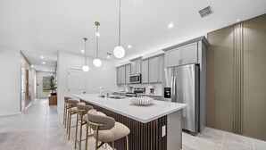 Una cucina moderna con isola centrale, sgabelli da bar, elettrodomestici in acciaio inossidabile e luci a sospensione.