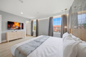 Ein modernes Schlafzimmer mit einem großen Bett, einem Flachbildfernseher, einer Kommode und Blick auf ein Gebäude.