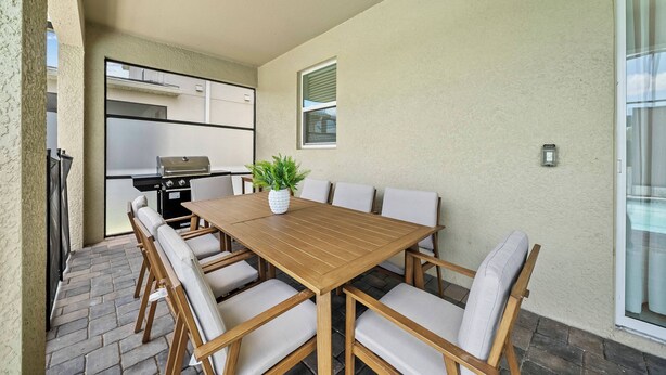 A patio with a wooden table and chairs, a grill, and a potted plant. - 7BR house sleeps 20 with hot tub and pool (Kissimmee)