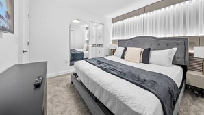 A modern hotel room with a large bed, a TV, and a bathroom visible through an archway. - 7BR house sleeps 20 with hot tub and pool (Kissimmee)