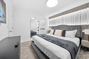 A modern hotel room with a large bed, a TV, and a bathroom visible through an archway. - 7BR house sleeps 20 with hot tub and pool (Kissimmee)