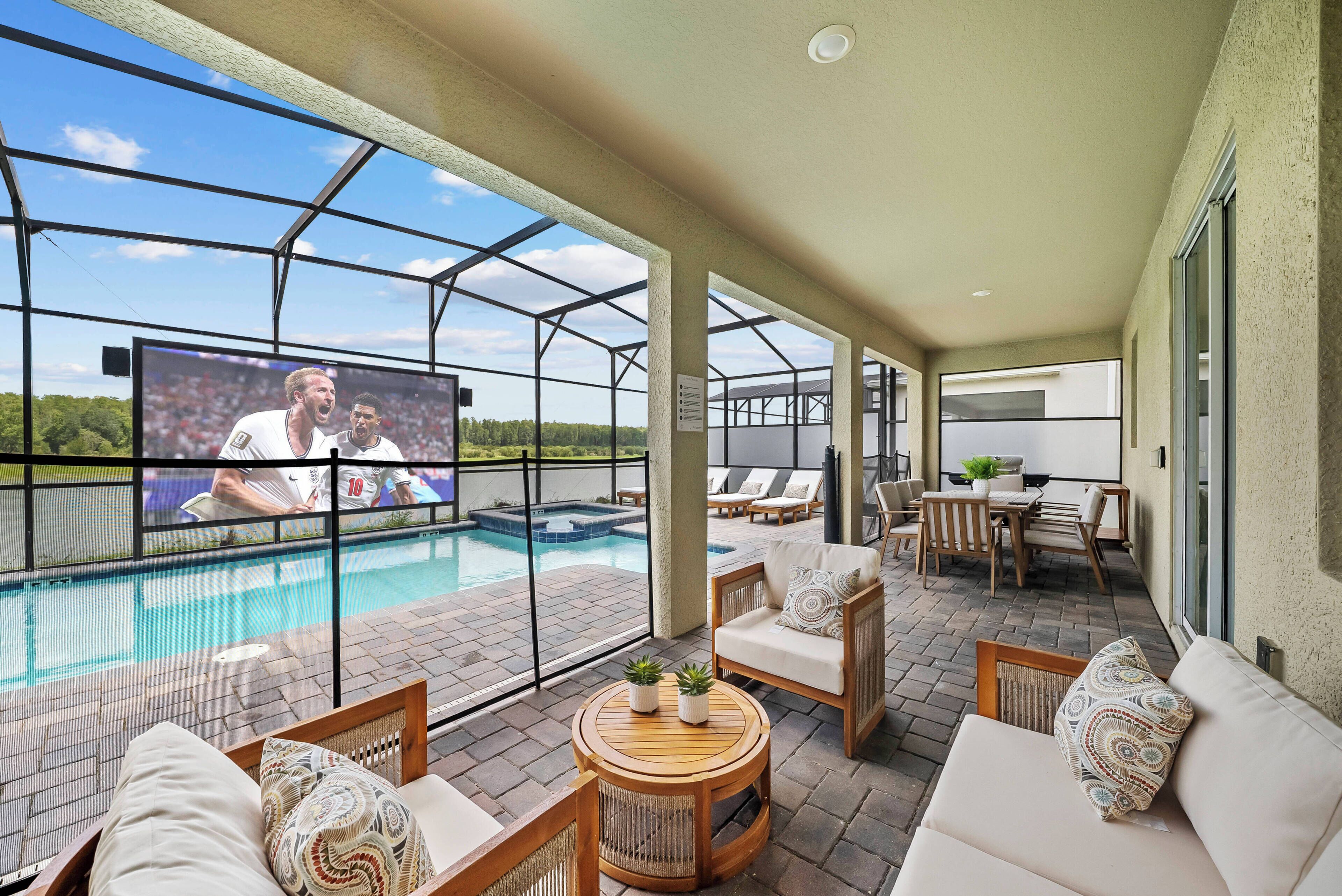 A covered outdoor area with a pool, seating, and a TV screen.
