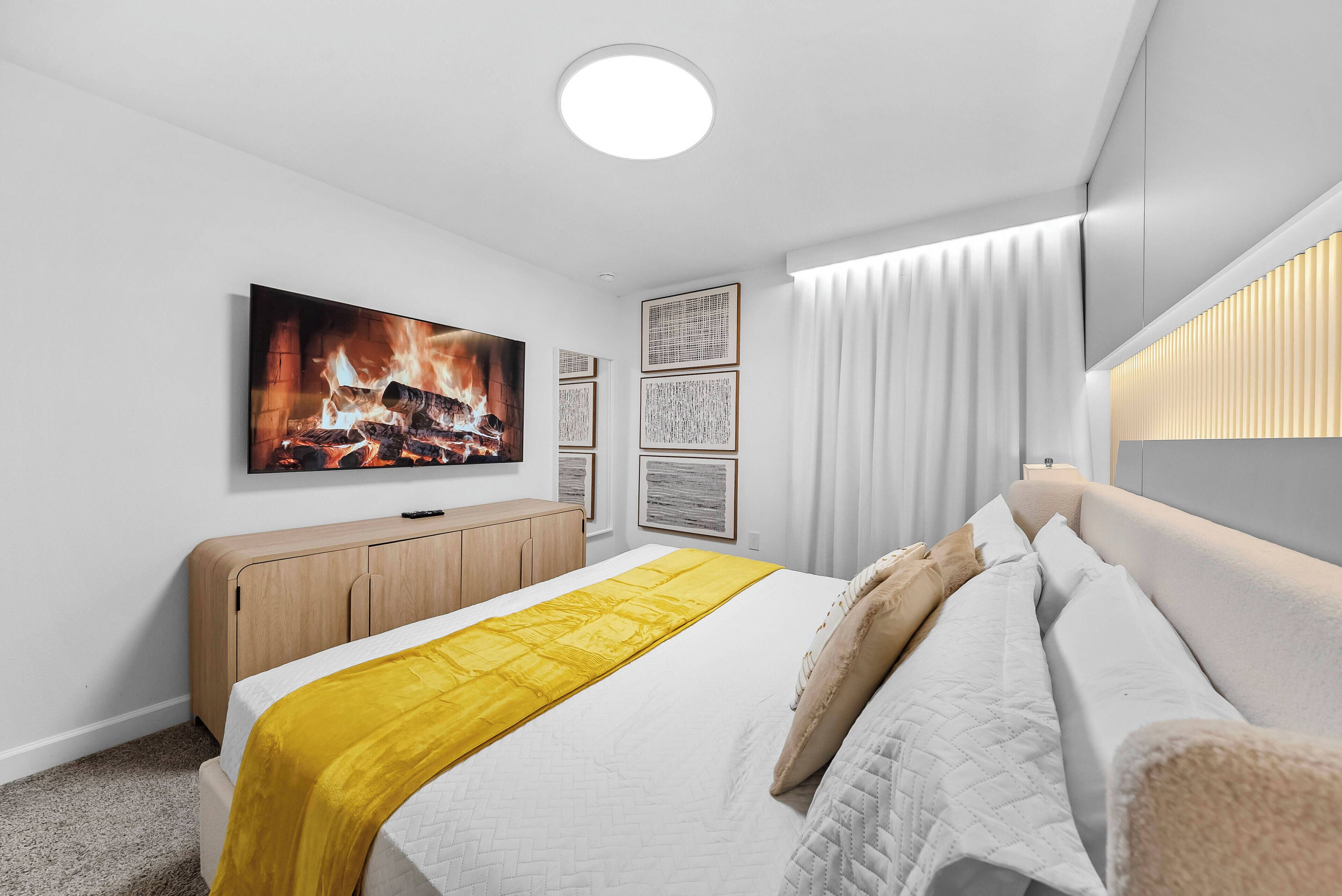 A modern bedroom with a bed, a TV mounted on the wall, a bedside table, and a window with curtains.