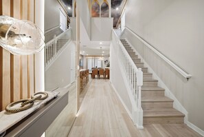 A spacious hallway with a wooden floor, a staircase with white railings, and a dining area in the background. - 7BR house at Windsor Cay Resort near Disney (Clermont)