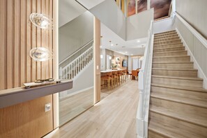 Un interno moderno con una scala in legno, una zona pranzo con sgabelli da bar e illuminazione a sospensione.