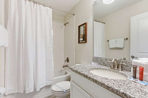 Step into a bright and well-appointed bathroom featuring a sleek granite countertop and modern fixtures. The soft white shower curtain and towels add a touch of freshness, creating a clean and comfortable atmosphere for your stay. - 6BR house with hot tub near Disney (Kissimmee)