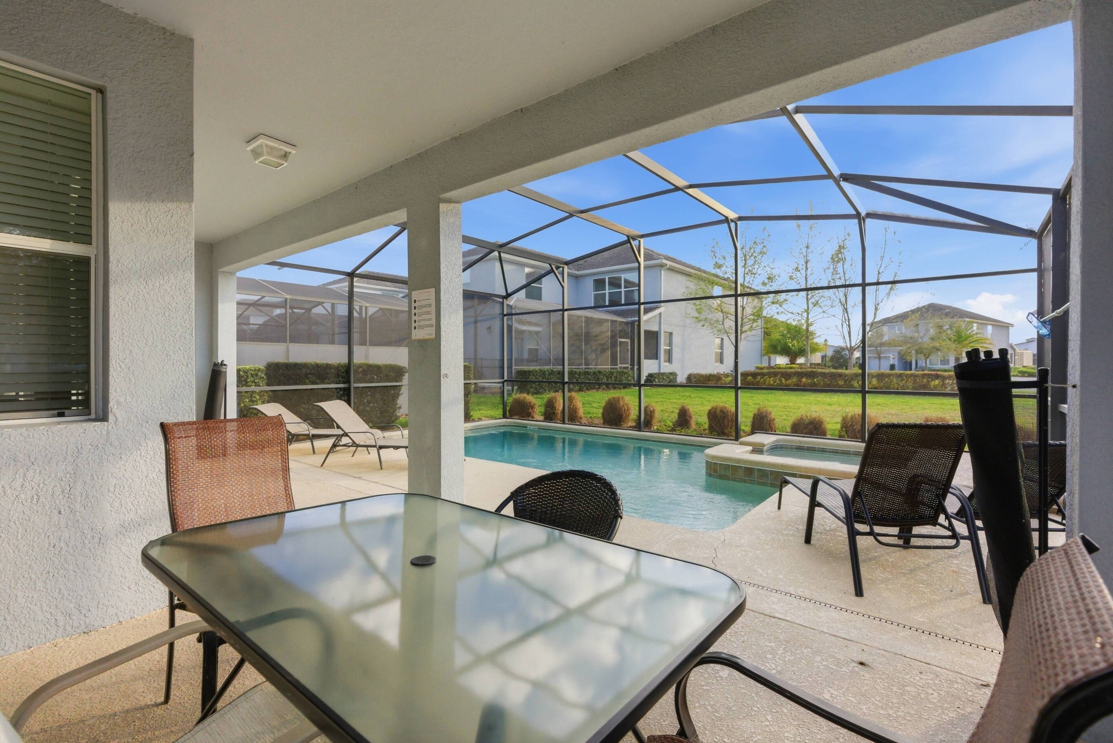 Experience your outdoor oasis with sunlight streaming through the screened lanai, highlighting the inviting dining table and cozy lounge chairs. Take refreshing dips in the sparkling pool, surrounded by tranquil greenery.