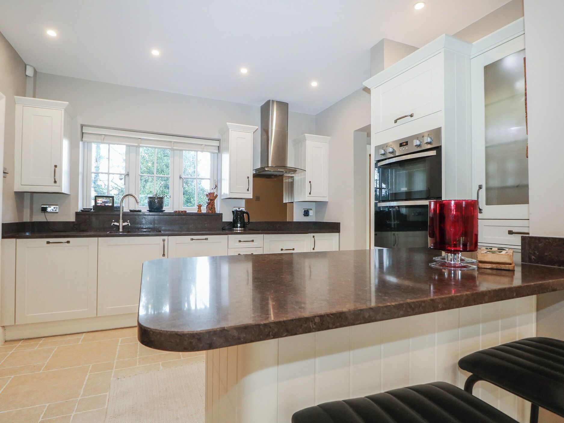 A modern kitchen with white cabinets, a stainless steel range hood, and a large island with a red candle.