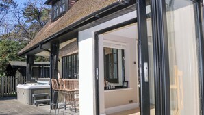 A modern house with a glass door leading to a patio area with outdoor furniture. - Woodlands House (Ringwood)