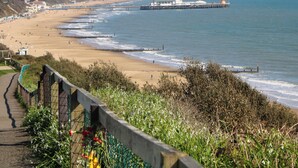 A coastal beach with a promenade, a lighthouse, and buildings in the background. - Woodlands House (Ringwood)