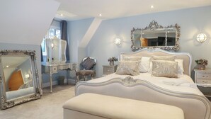 A bedroom with a large bed, a vanity with a mirror, and a chair. - Woodlands House (Ringwood)