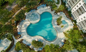 Una vista aerea di un resort con una piscina centrale circondata da lettini prendisole e palme.