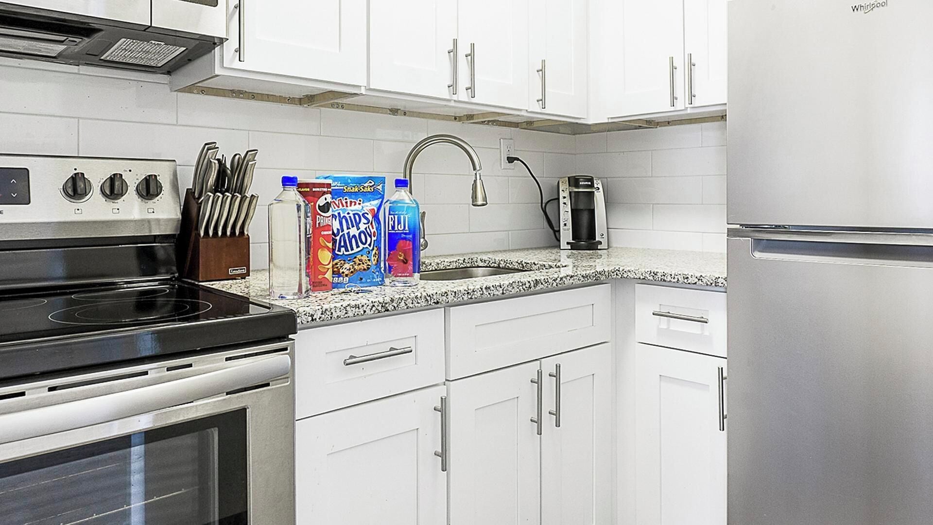 A kitchen with white cabinets, a stainless steel refrigerator, a stove, and a coffee maker.