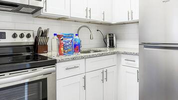 A kitchen with white cabinets, a stainless steel refrigerator, a stove, and a coffee maker.