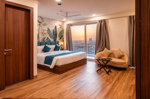 Una habitación de hotel moderna con una cama grande, un sofá, una mesita y un balcón con vistas a la ciudad.