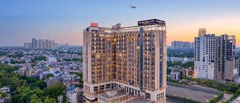 A multi-story hotel with a prominent sign, surrounded by a cityscape and greenery.