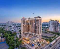 Un hotel de varios pisos con un letrero llamativo, rodeado de paisaje urbano y zonas verdes.