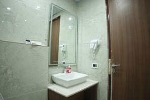 Un bagno con parete in marmo, lavandino bianco, specchio, asciugacapelli e porta in legno.